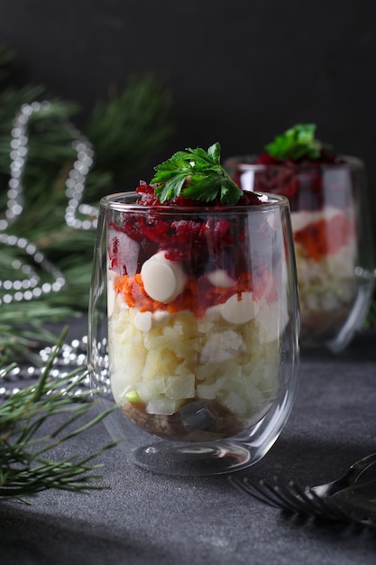 Traditionele Russische feestelijke salade Haring onder een bontjas in geportioneerde glazen op een donkergrijze achtergrond