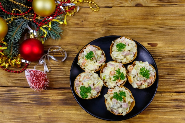 Traditionele Russische feestelijke salade Olivier in taartjes en kerstversiering op houten tafel. Bovenaanzicht