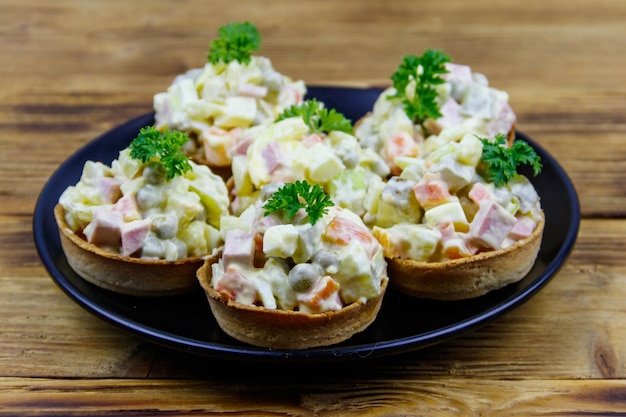 Traditionele Russische feestelijke salade Olivier in tartlets op een houten tafel