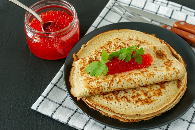 Traditionele russische pannenkoeken blini gestapeld in een bord met rode kaviaar op houten achtergrond. maslenitsa traditionele russische festivalmaaltijd. russisch eten, russische keuken. detailopname.