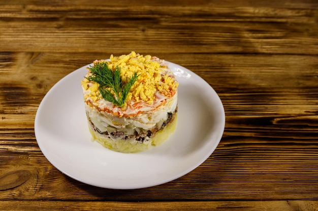 Traditionele Russische salade Mimosa op houten tafel. Gelaagde salade met sardine, ui, aardappelen, wortel, kaas, eieren en mayonaise