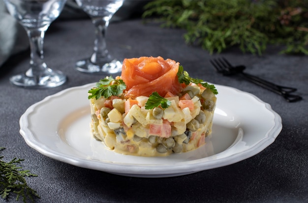 Traditionele Russische salade Olivier met gezouten zalm op een donkere achtergrond. Feestelijke presentatie.