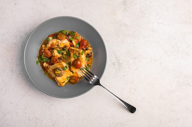 Traditionele Siciliaanse vis met tomaten, olijven, peterselie en rode paprika in een diepe plaat met vork op