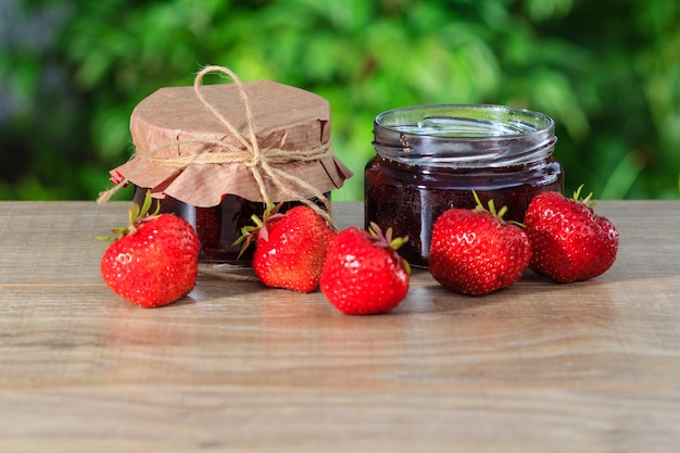 Traditionele zelfgemaakte aardbeienjam in potten, versierd met verse aardbeien op houten tafel met groene wazige natuurlijke achtergrond natural