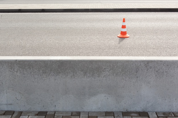 Traffic cone on bitumen pavement road for cars with a large concrete fence separating the road and sidewalk