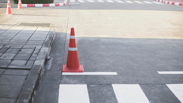 A traffic cone is on the road in front of a drain