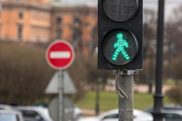 A traffic light for pedestrians with a symbol of a walking person is lit with a green light and a si