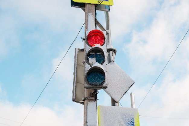 Traffic light and road sign on pole covered with snow after snowstorm on winter day