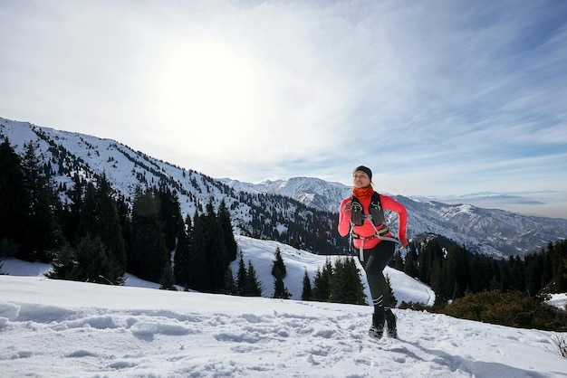 雪の上の冬の山で走っているトレイルランナーの女性トレイル女性アスリートランナーの側面図で上り坂を走るダイナミック