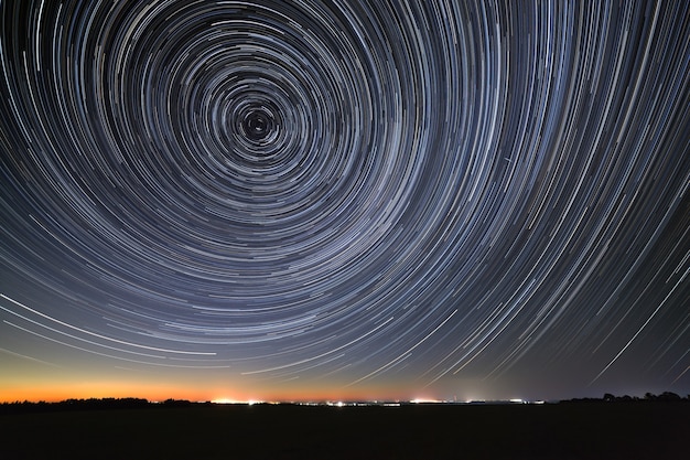 След звезд на ночном небе отражается в реке. Движение в космосе сфотографировано на длинной выдержке.