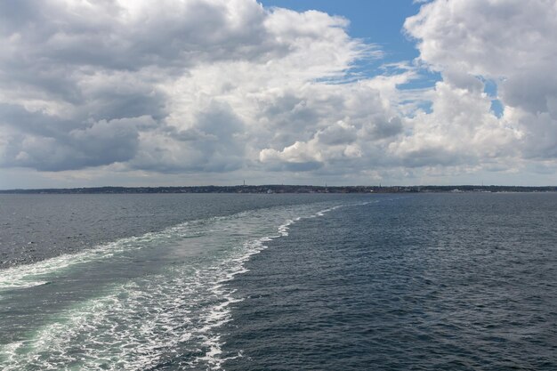 Photo trail in the water left by a ferry moving away from the shore with houses