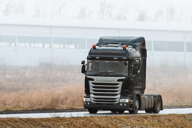 Trailerless tractor unit on the highway A truck gleams under the soft sunlight as it travels along a quiet road bordered by wild grass and a distant building Modern powerful truck cabin