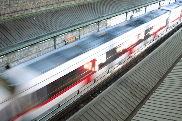 A train is passing by a building with a red stripe.