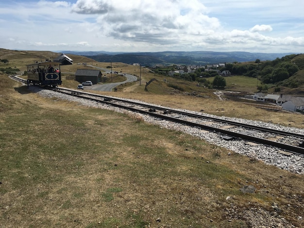 Photo train on railroad track against cloudy sky during sunny day