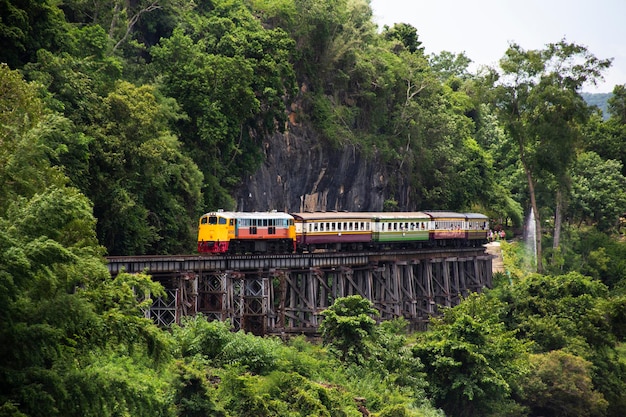 Train running on track between hellfire pass mountain and riverside Sai Yok waterfall and Khwae river bring thai people and foreign travelers travel visit at Tham krasae cave in Kanchanaburi Thailand