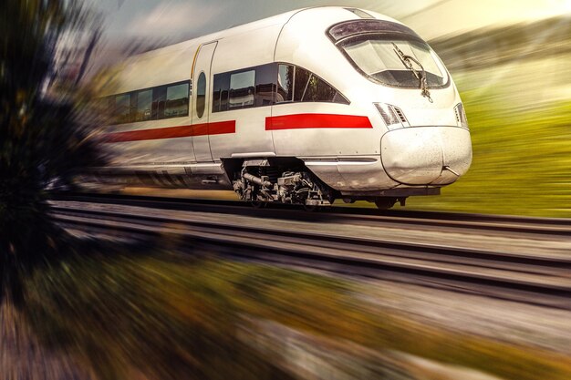 Foto il treno corre veloce su rotaie con motion blur sotto il sole splendente e la natura verde