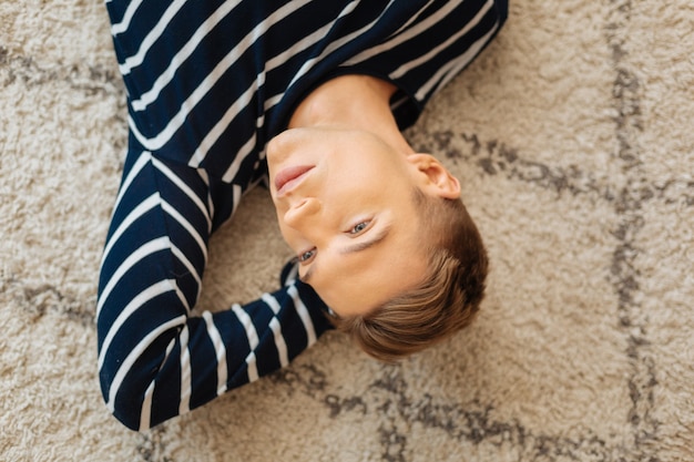 Train of thoughts. Handsome thoughtful fair-haired well-built young man lying on the floor and thinking and looking in the distance