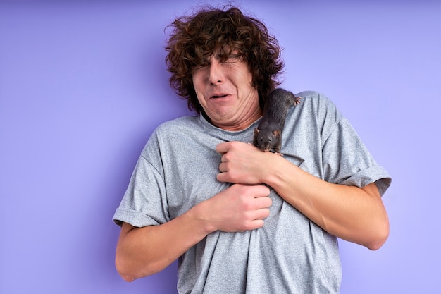 Trained decorative rat climbs on man's t-shirt, crawling. male is confudes and scared, stand at a loss, can't move