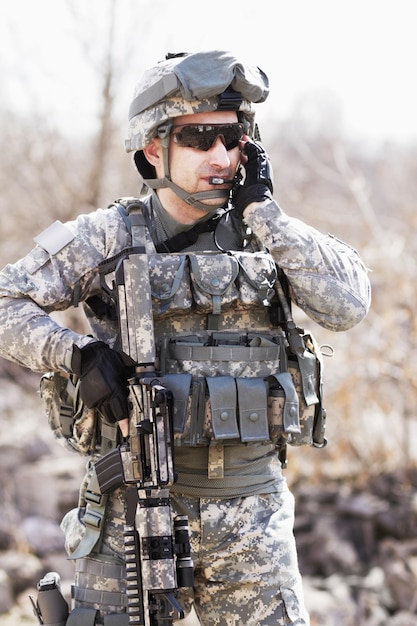 Trained in military tactics. A soldier crouched down next to a broken down wall and pointing his gun into the distance.