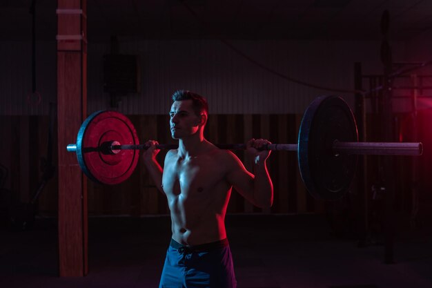 Trainen door gewichten op te heffen in een crosstraining sportschool Gespierde krachtige man met zware barbell in rood blauw neonlicht