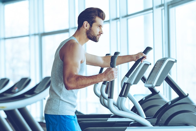 Trainen voor het beste lichaam. Zijaanzicht van een jonge knappe man in sportkleding die wegkijkt terwijl hij aan het trainen is op de stepper in de sportschool