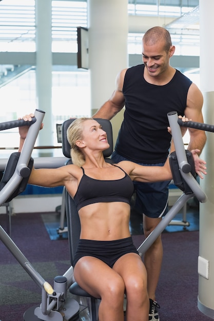 Trainer assisting woman on fitness machine at gym