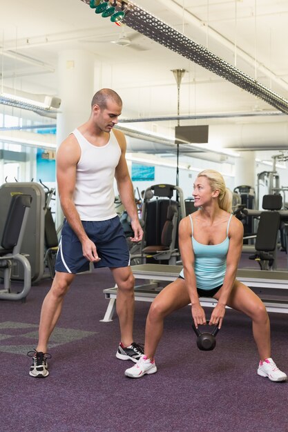 Trainer assisting woman with kettle bell in gym