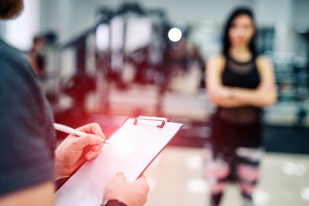 Trainer and client discussing her progress at the gym Gym instructor writing on clipboard