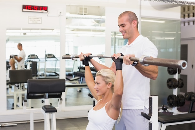 Trainer die vrouw met het opheffen van barbell in gymnastiek helpen