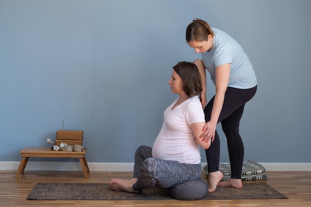 Trainer die zwangere vrouw helpt om yogaasana voor schouders en borst te doen,