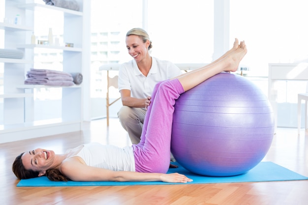 Trainer helping woman with exercise ball