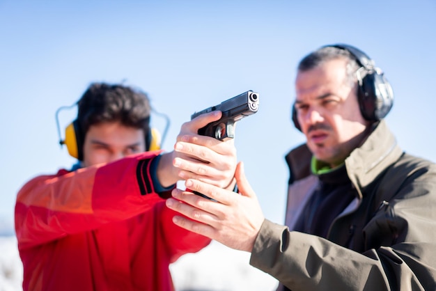 Тренер помогает молодому человеку целиться из пистолета во время боевой подготовки. Фото высокого качества