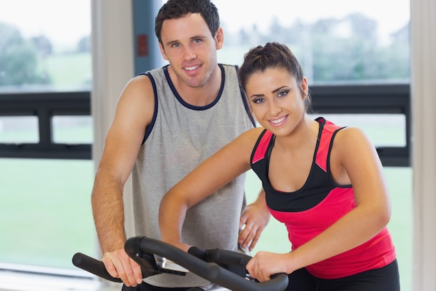 Trainer helping young woman work out at spinning class