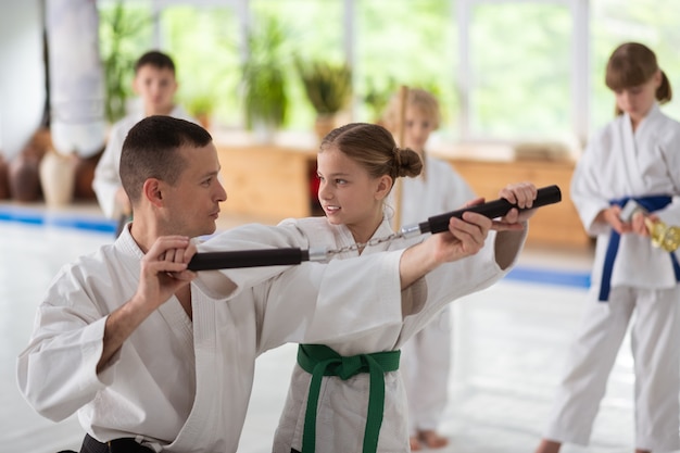Trainer helpt. Donkerharige aikido-trainer die spreekt en meisje helpt nunchucks te gebruiken