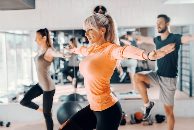 체육관에서 그룹 균형 운동을 보여주는 트레이너. 백그라운드에서 거울 반사. 금발 여자에 선택적 초점입니다.