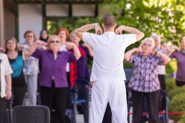 trainer training motivated active healthy senior people to performing exercise in the park