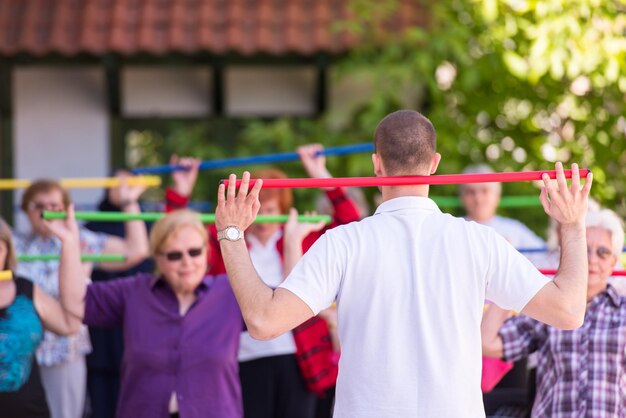 trainer training motivated active healthy senior people to performing exercise in the park