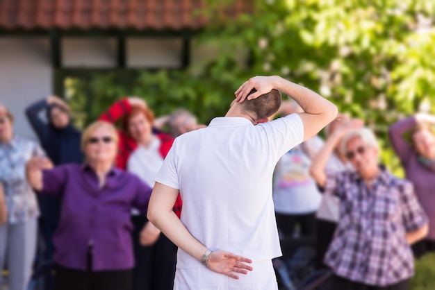 trainer training motivated active healthy senior people to performing exercise in the park