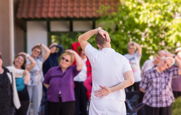 trainer training motivated active healthy senior people to performing exercise in the park