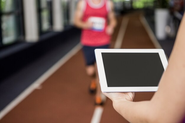 Trainer using a digital tablet while man performing running exercise