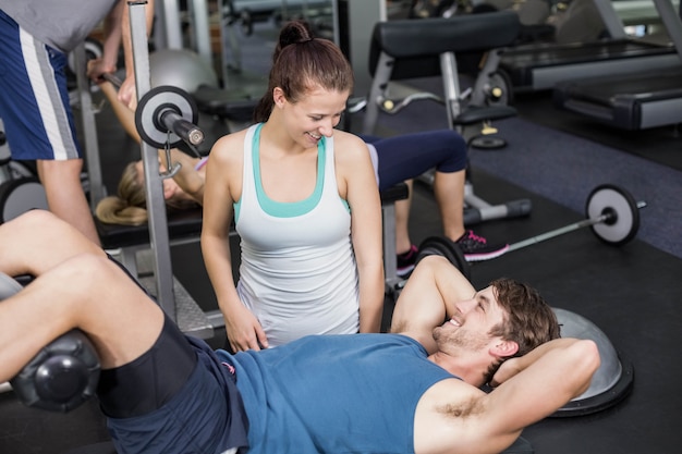 Trainer woman helping man doing his crunches at gym