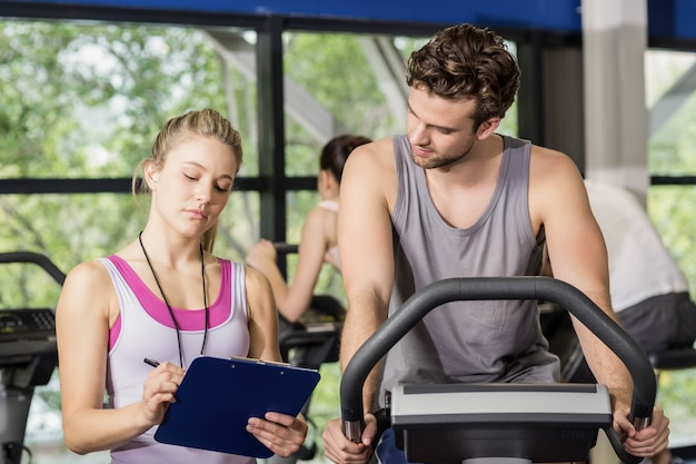 Trainervrouw die met een mens spreken die hometrainer doen bij gymnastiek