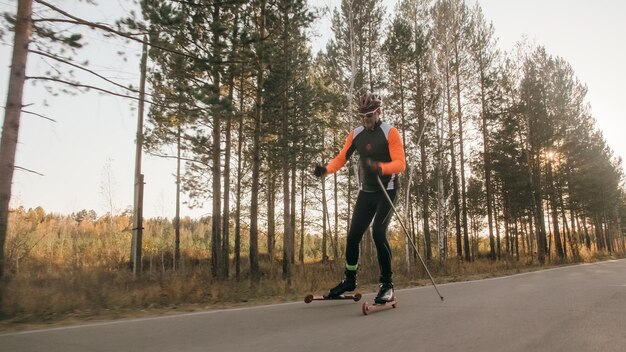 Training an athlete on the roller skaters biathlon ride on the\
roller skis with ski poles in the helmet autumn workout roller\
sport adult man riding on skates