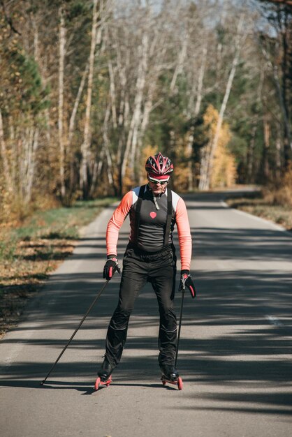 Training an athlete on the roller skaters biathlon ride on the\
roller skis with ski poles in the helmet autumn workout roller\
sport