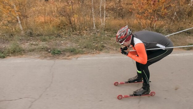 Training an athlete on the roller skaters Biathlon ride on the roller skis with ski poles in the helmet Autumn workout Roller sport