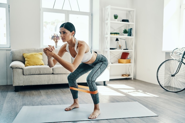 Training to become the best. Full length of beautiful young woman in sports clothing crouching while exercising at home