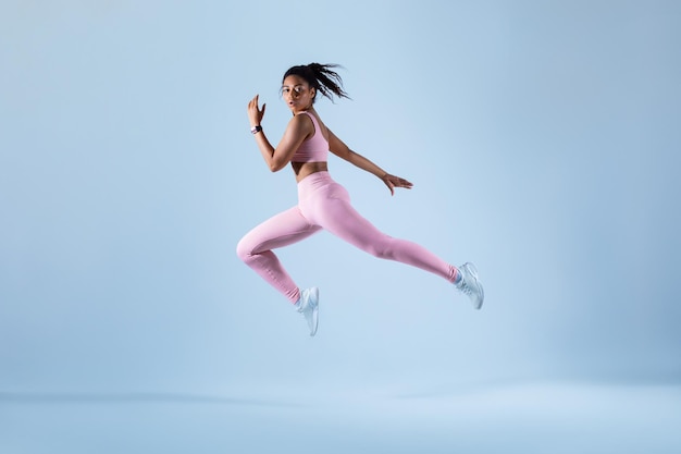 Photo training concept fit black woman in sportswear jumping or running exercising on neon blue studio background