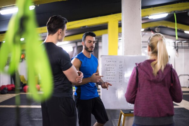 Training course.group of young athletes getting instructions\
from trainer before exercise at cross fitness gym