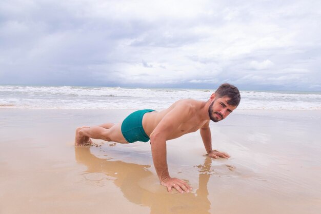 Training exercise Closeup Of Healthy Handsome Active Man With Fit Muscular Body Doing Push Ups Exercises Athletic male sport exercise on the beach training outdoors Sports and Fitness Concept