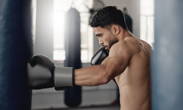 Training fitness and workout man boxer sweating and doing a cardio exercise at the gym Sporty sweaty and determined male athlete punching a bag at a sports boxing center for health and wellness